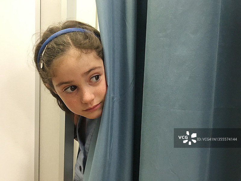 害怕地躲在窗帘后面的年轻女孩图片素材