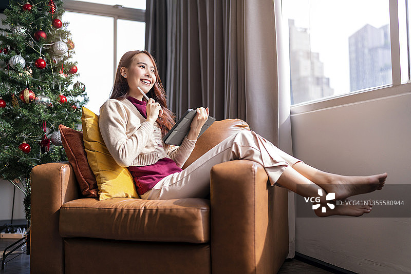 亚洲女性在客厅沙发上使用平板电脑记录工作，度过圣诞假期图片素材