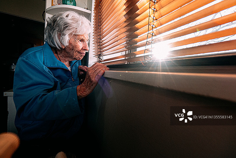 在室内透过百叶窗向外看的老年白人妇女图片素材