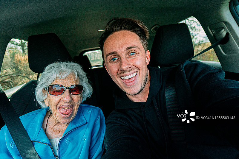 可爱的祖母和年轻成年孙子坐在汽车前排座位上一起旅行或跑腿的自拍图片素材