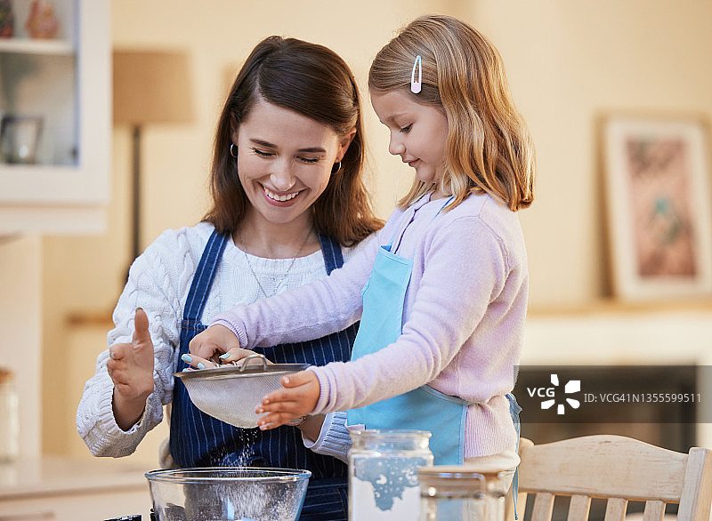年轻母亲帮助女儿将面粉筛入碗中图片素材