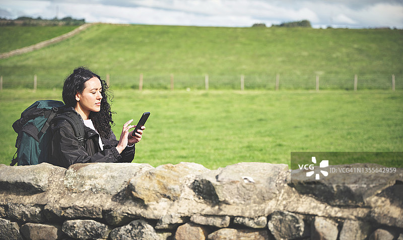 年轻女子在乡村背包旅行时沉思地看着手机图片素材