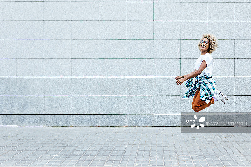 在城市街道的墙边跳跃的快乐非洲裔美国女人图片素材