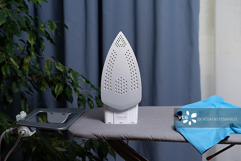 熨衣板上叠放的鲜艳干净的彩色熨烫衣物，旁边有电熨斗。家庭作业的概念，缺乏做家务的时间。妇女的职责，家庭生活。日常生活。图片素材