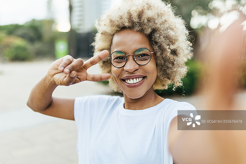 在户外街上自拍时做出和平手势和微笑的非裔美国女人图片素材