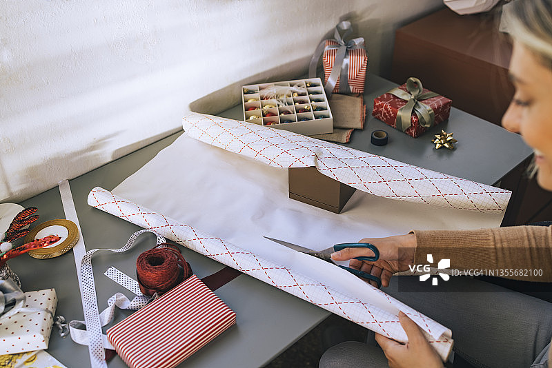 微笑的金发女人正在裁剪包装纸以包装圣诞礼物图片素材