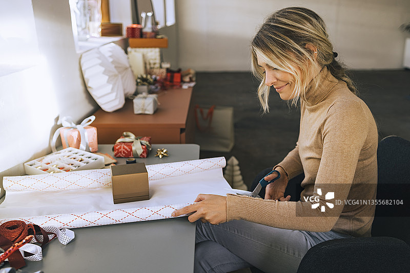 一位女士用剪刀剪裁包装纸来包装圣诞礼物的侧面照图片素材