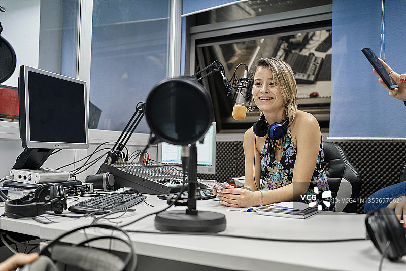 美丽的女主持人坐在广播演播室的麦克风前，看着同事微笑图片素材