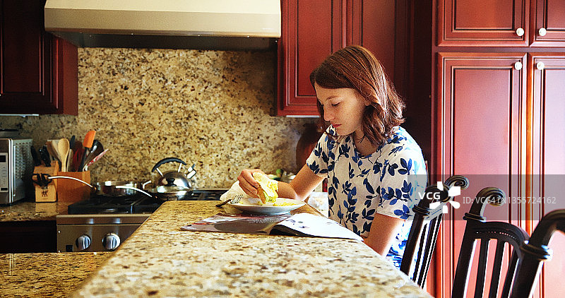 在厨房岛台上吃鸡蛋吐司的少女图片素材