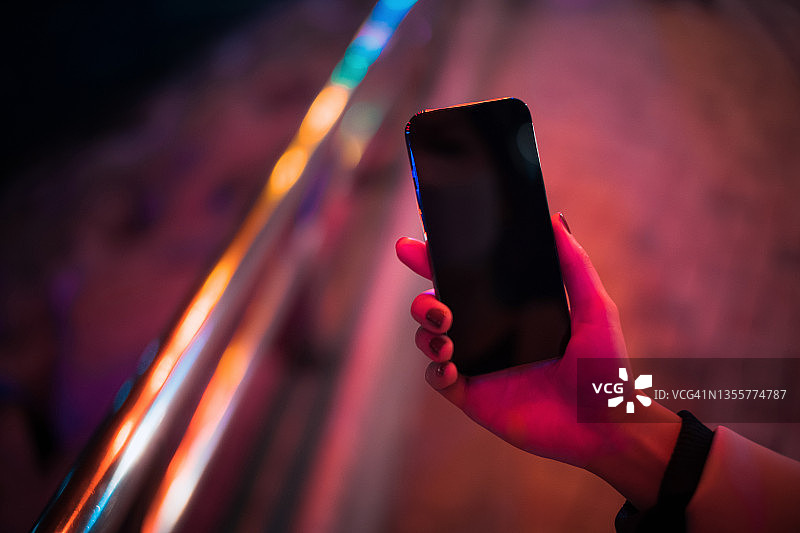 夜晚繁华都市街道，红光下的女人使用智能手机。手机屏幕样机图片素材