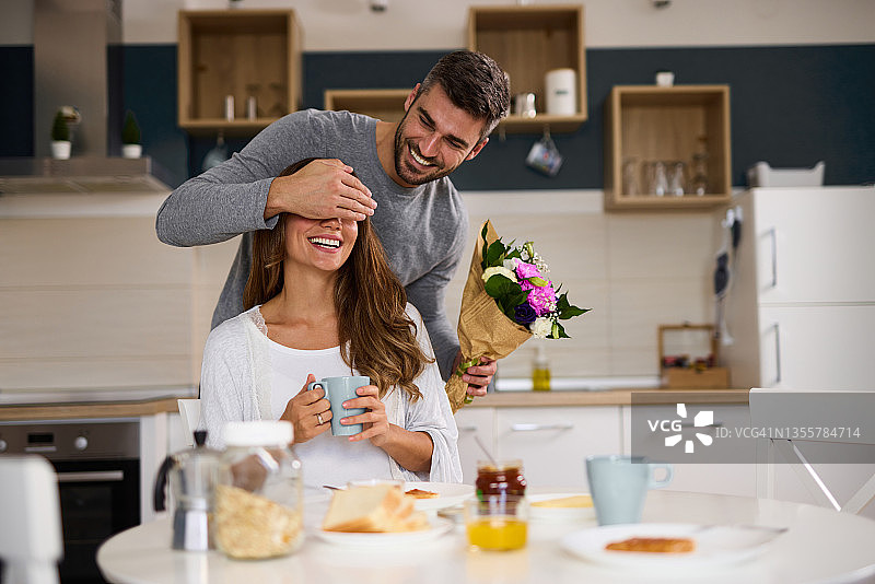 男人用手捂住妻子的眼睛，想给她一个惊喜，在家里送她一束鲜花图片素材