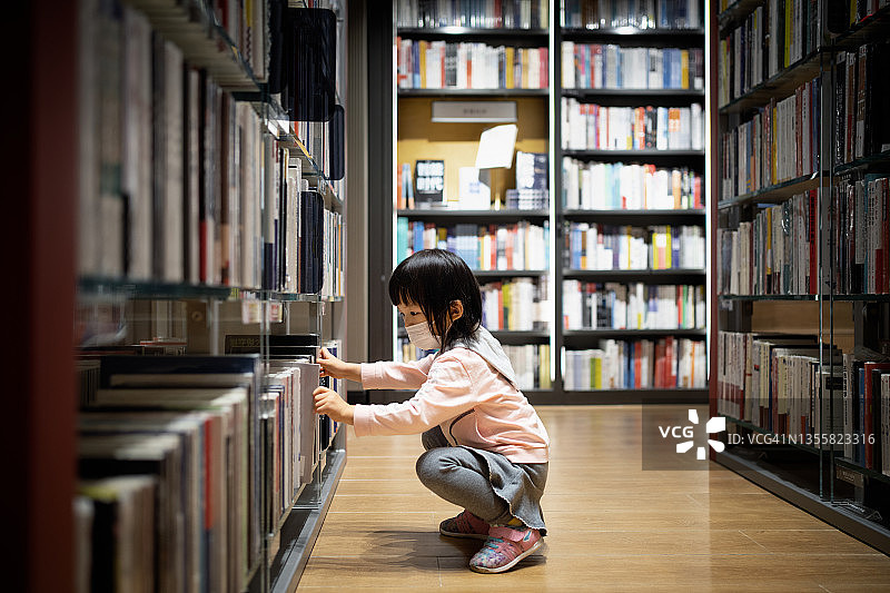 在书店里寻找和阅读书籍的3岁小女孩图片素材