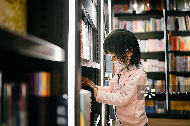 在书店里寻找和阅读书籍的3岁小女孩图片素材