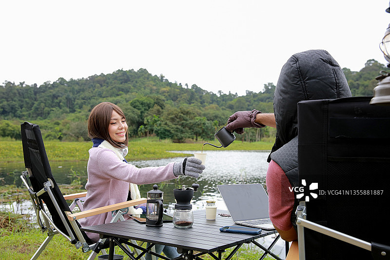 快乐的夫妇在露营旅行时在湖边山丘旁喝咖啡图片素材