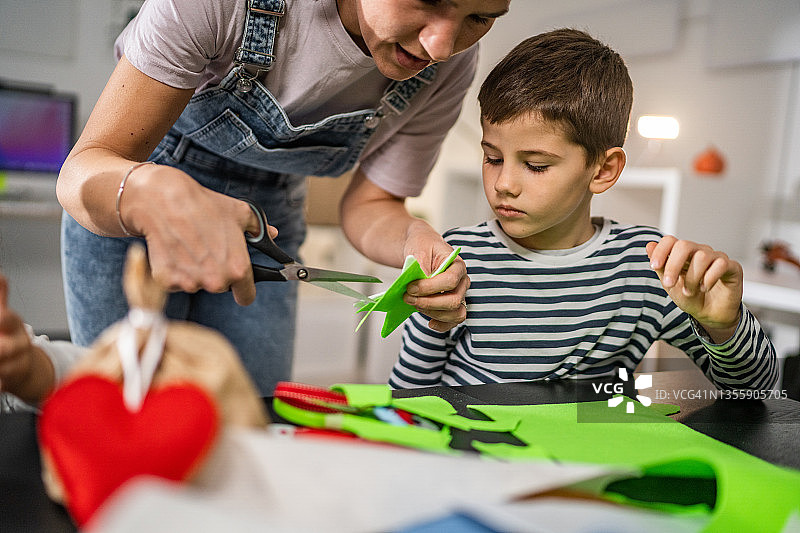 母亲和儿子用剪刀剪纸制作圣诞卡图片素材