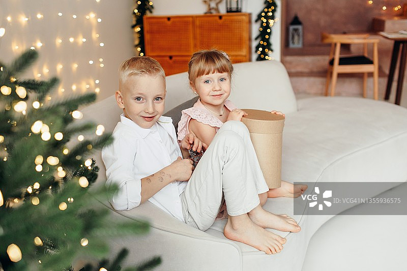 孩子们的圣诞照片：圣诞树旁有礼物的兄妹，圣诞节和新年概念图片素材