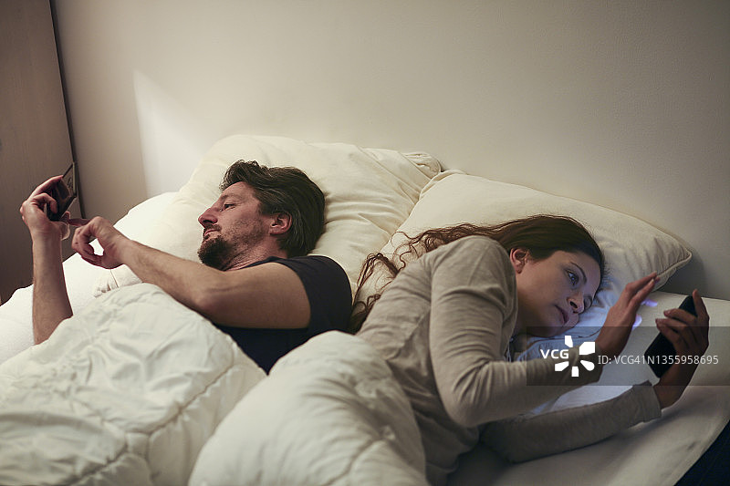 床上情侣被智能手机隔开图片素材