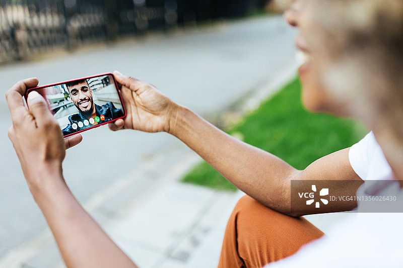 坐在街上，用手机和男友视频聊天的拉丁裔年轻女子图片素材