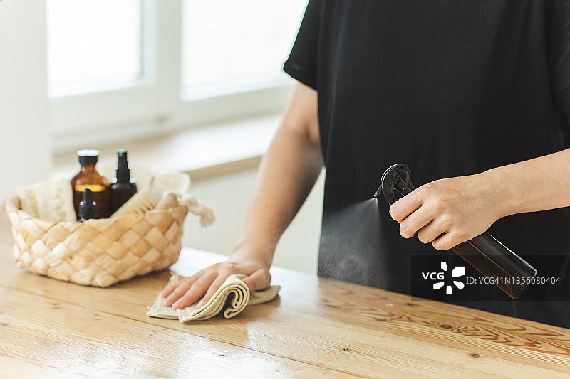 女人用喷雾和天然织物清洁剂擦拭脏桌子上的灰尘图片素材