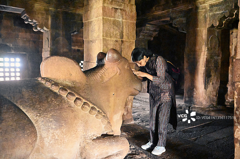 在卡纳塔克邦埃霍莱古印度教石窟寺庙中向南迪祈祷的女人图片素材