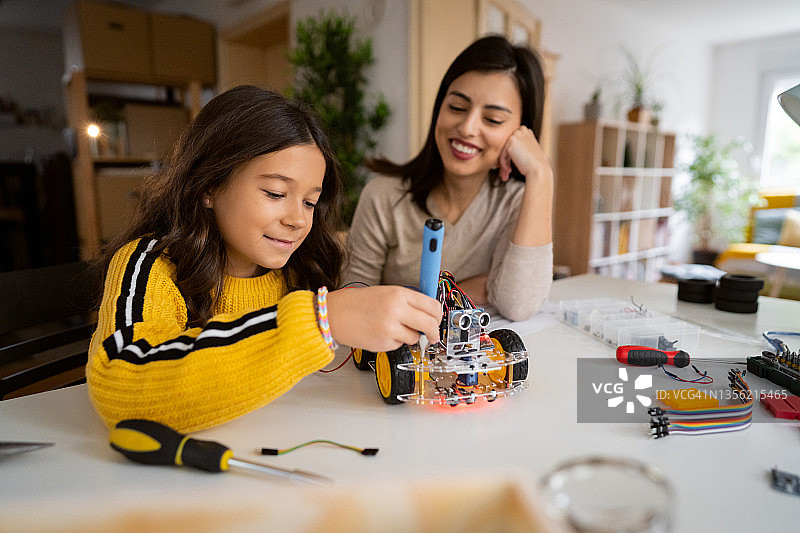 一位自豪的母亲笑着观察她聪明的女儿，她正在制造一辆自动驾驶的机器人汽车图片素材