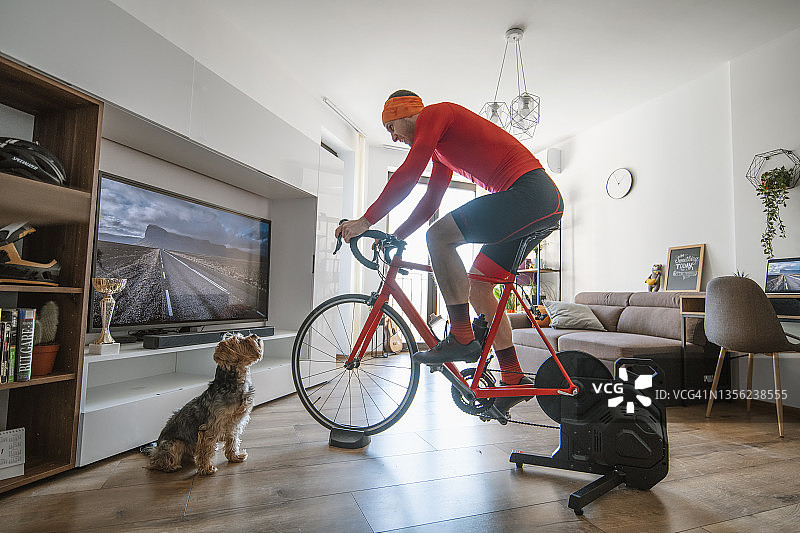 男人在家骑自行车，他的狗看着他图片素材