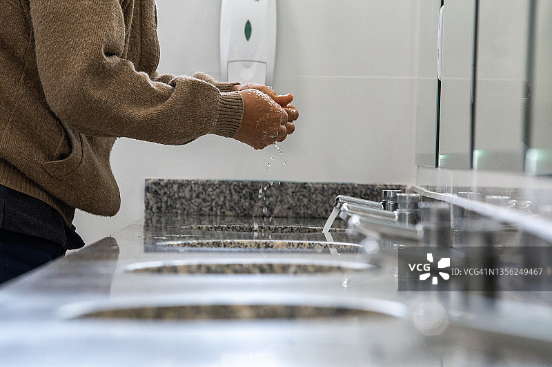 男子在公共浴室的水槽里洗手图片素材