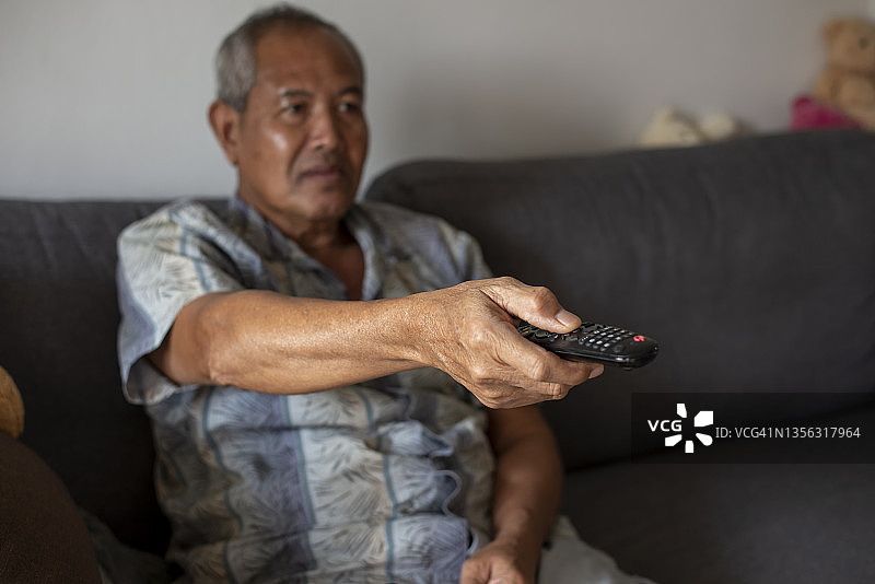 老人手持遥控器换电视频道，坐在沙发上看电视图片素材