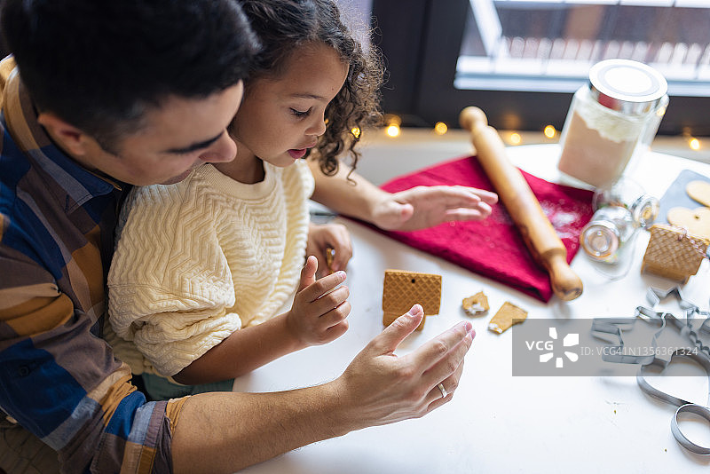 女孩和父亲一起制作圣诞姜饼屋饼干图片素材