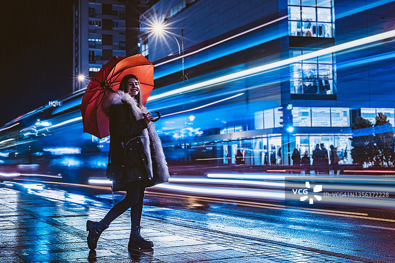 快乐的女人在市区打着伞长曝光图片素材