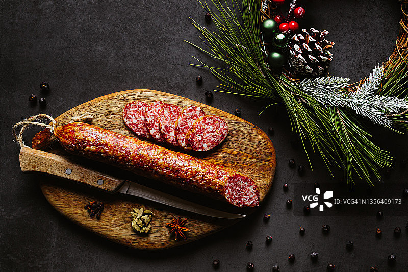 自制萨拉米香肠的圣诞节低调扁平摆放，配以杜松子、小豆蔻、丁香、八角、菜刀和圣诞装饰图片素材