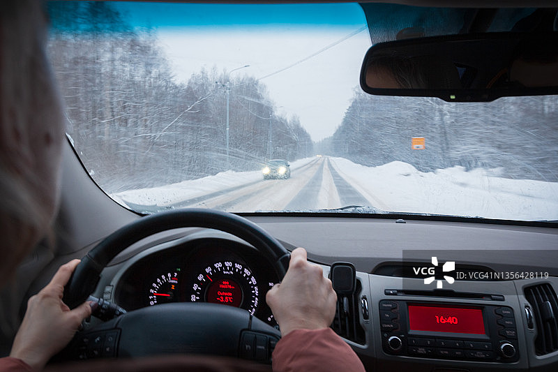 驾驶员手握方向盘，汽车仪表盘背景为冬季沥青路面图片素材