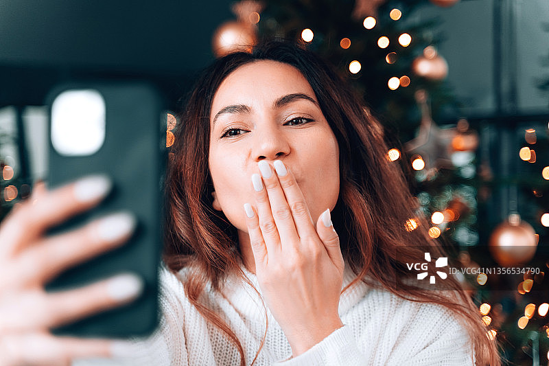 年轻漂亮的女人通过视频聊天祝朋友们圣诞快乐或自拍图片素材