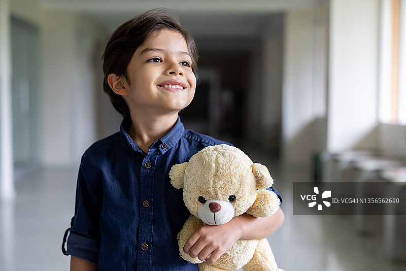 快乐的男孩在医院里抱着泰迪熊微笑图片素材