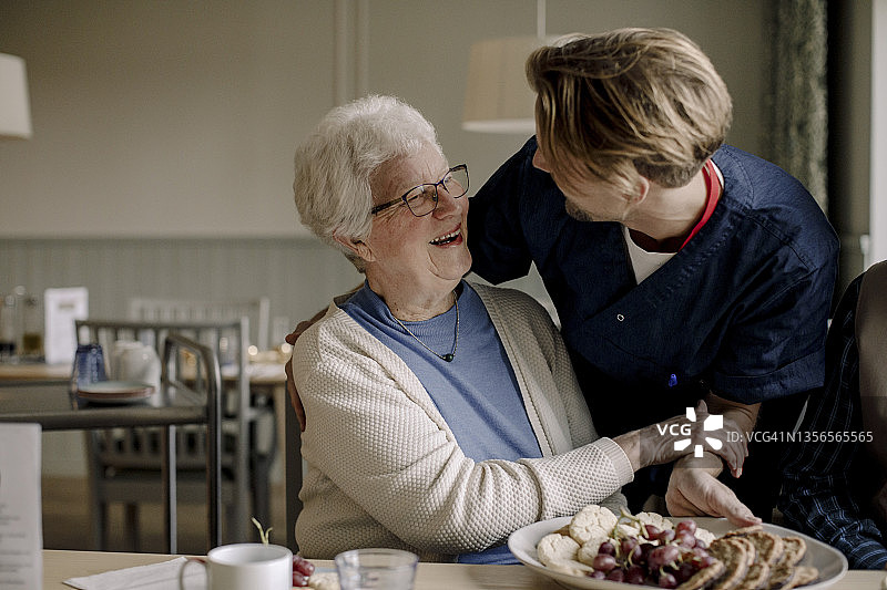 快乐的老年妇女在养老院与提供食物的男护士交谈。图片素材