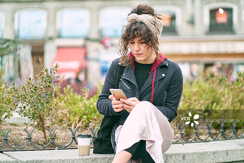 专注的女性在街上咖啡附近浏览智能手机图片素材