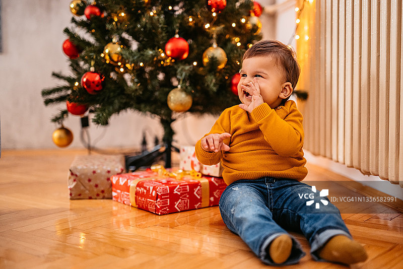 男孩坐在圣诞树下，周围都是礼物图片素材