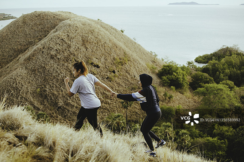 亚洲穆斯林女子和朋友在日出时分在山上看海滩图片素材