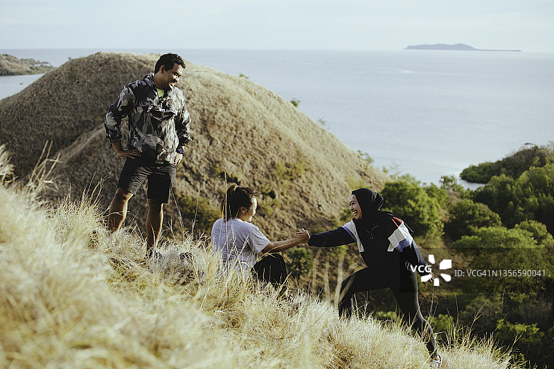 在日出时分于山丘上眺望海滩的亚洲青年图片素材