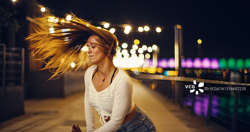 年轻女人在潮湿的城市街道上充满活力地跳自由舞。甩着头发图片素材