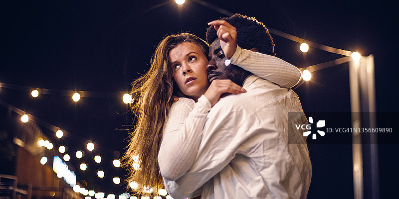 年轻多元的情侣在潮湿的城市街道上表演感性舞蹈，夜晚浪漫场景，专注于面部表情图片素材