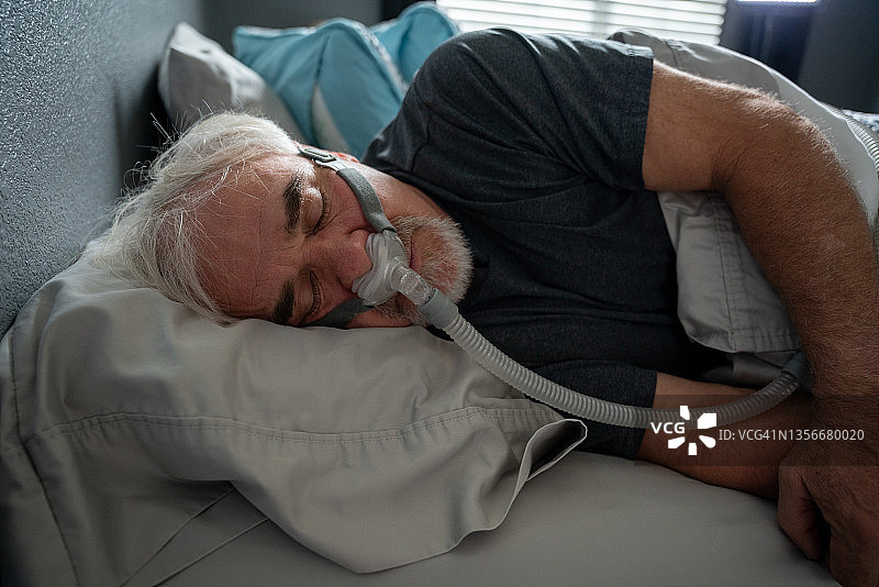 患有睡眠呼吸暂停的年长男人在床上戴着CPAP面罩睡觉图片素材