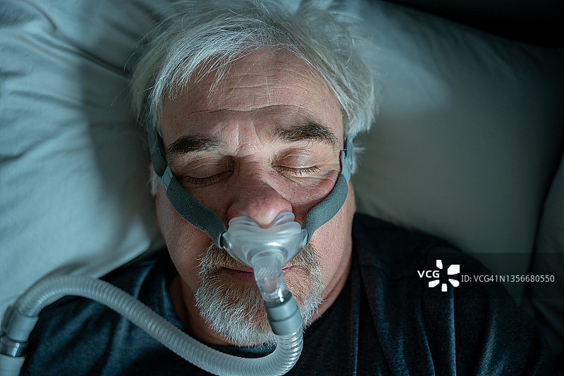 患有睡眠呼吸暂停的年长男人在床上戴着CPAP面罩睡觉图片素材