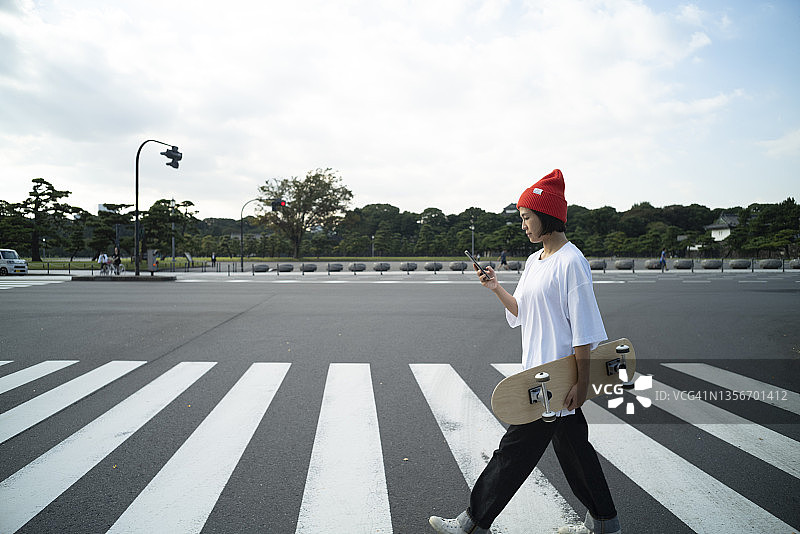 女人踩着滑板穿过人行横道图片素材