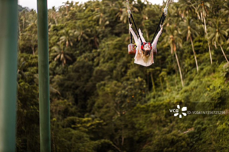 年轻快乐的女人在雨林上荡秋千图片素材