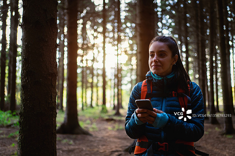 担忧的白人年轻女子在森林徒步时，使用手机导航图片素材