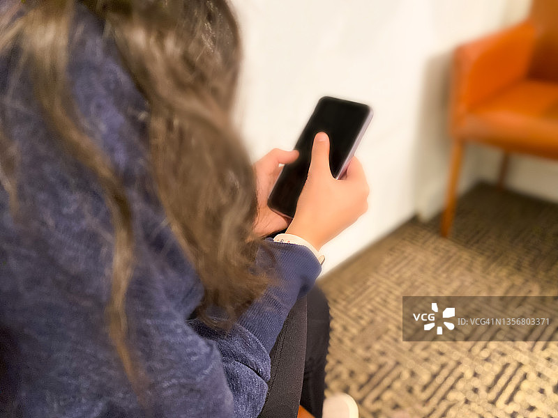 年轻混血女子在医生候诊室里拿着智能手机图片素材