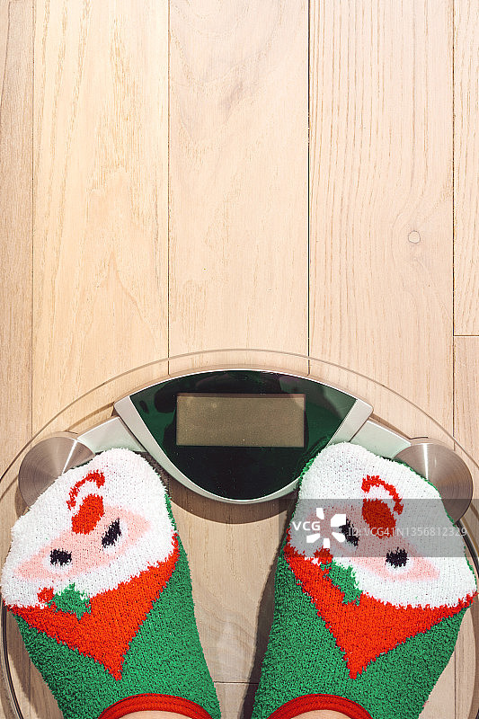 穿着圣诞趣味红绿雪人袜站在体重秤上的女人，新年假期体重超重问题图片素材