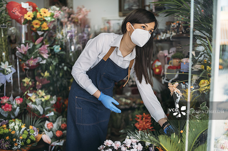 戴口罩的年轻女人在花店里整理鲜花图片素材