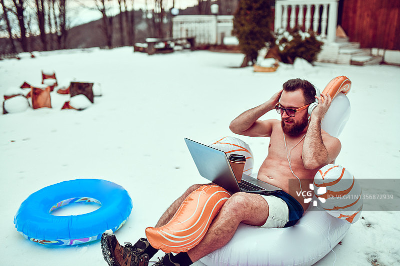 在雪山沙滩充气玩具上听音乐的微笑男人图片素材